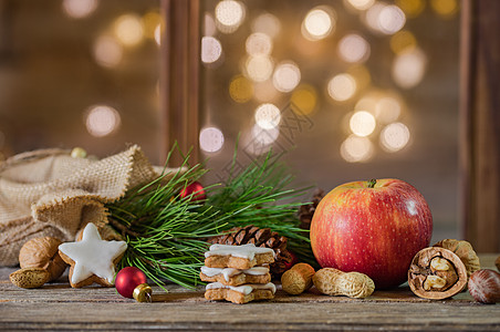 圣诞假日背景 红苹果 饼干和芬果树枝 在灯光模糊的木柴上用圣塔袋袋装图片