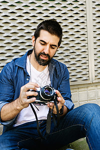 使用相机检查时坐在地上的胡子旅行者男子的身旁 夏天 假期图片