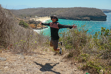 一个年轻人在沙滩上跳跃 玩得开心 暑假度假的生活方式 快乐的少年跳跃自由 穿着短裤和 T 恤的亚洲人在悬崖上跳跃 天空 美丽的图片