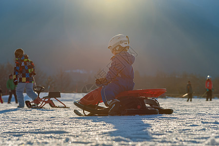 孩子从山上下来 骑着红色雪橇图片