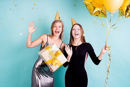 两个戴着生日帽子的年轻女青年 拿着气球 在蓝底上庆祝生日 幸福 蓝色的图片