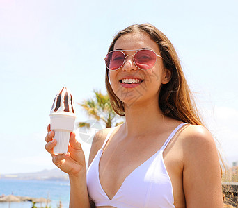 拿冰淇淋女孩夏日假期在海滩上吃冰淇淋的太阳眼镜女孩的肖像背景