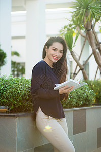 在阳光明媚的日子里 站在校园咖啡馆露台上微笑的女学生看书的画像 教育 生活方式和人们的观念 阳台 户外的图片