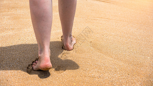 女人赤脚走在沙滩上 在夏季海滩上沿着海水和沙子的波浪行走的年轻女子的腿特写 旅游概念 走在沙滩上的女人在沙滩上留下脚印 旅行 假图片