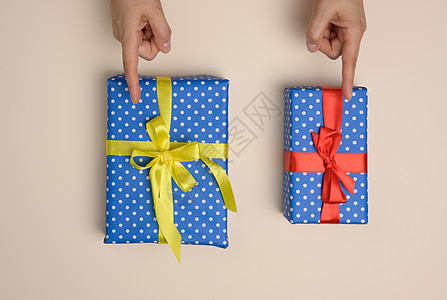 两盒装在蜜蜂背景上丝丝带的礼物盒 由女性手指表示选择图片