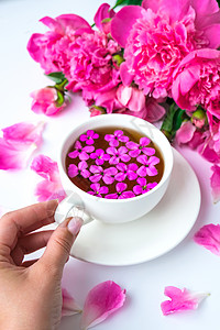 粉红色牡丹花的创意布局 女手拿着一杯茶放在明亮的桌子上 春季季节性情人节 女人 母亲 3 月 8 日假期 浪漫早餐 时尚博主 问图片