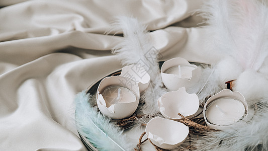 时髦的复活节装饰品 板上有裂纹的有机鸡蛋 鸡蛋白壳中的蜡烛 鸟羽 复制空间 问候卡 柔和的颜色 假期 复活节彩蛋图片