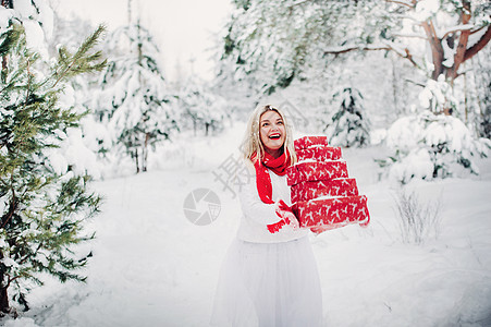 一个穿着白色毛衣 手里拿着圣诞礼物的女孩站在白雪覆盖的森林里 冬天外面拿着圣诞礼物的女人 圣诞节 女士图片