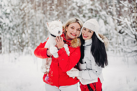 两个女孩和一条狗在寒冷的冬天森林里的画像 一个女孩在白雪皑皑的冬日森林里抱着一只狗图片