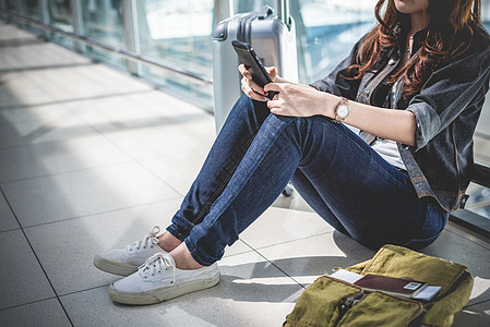 年轻女子坐在机场休息室等待出发时带着包和手提箱行李的特写 女性旅行者和旅游主题 旺季和假期的概念 放松和生活方式 女孩 周末图片
