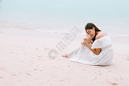 亚洲女人拥抱熊娃娃 等待让她在海滩上开心的爱情 孤独与美丽的概念 女孩的背影场景 海洋和海洋主题 复制左侧的空间 灵魂伴侣主题图片
