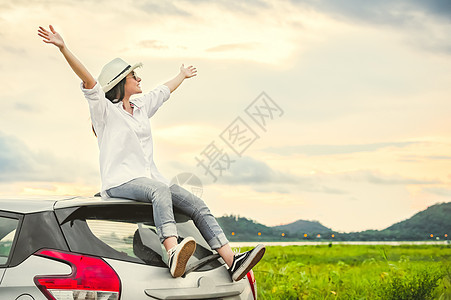 快乐的亚洲女人在日落后的车顶上张开双臂 带着幸福的心情呼吸新鲜空气 人们在长假旅行概念中的生活方式 户外自然与交通背景图片