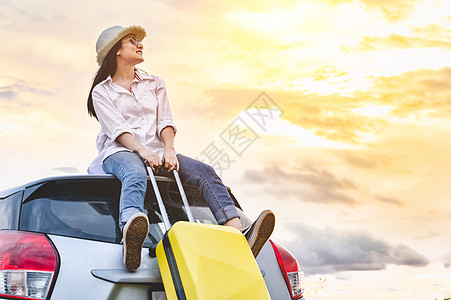 快乐的亚洲女人带着行李袋在车顶上 女孩坐在屋顶上 在傍晚前看日落 人们在长假旅行概念中的生活方式 自然和交通工具背景图片
