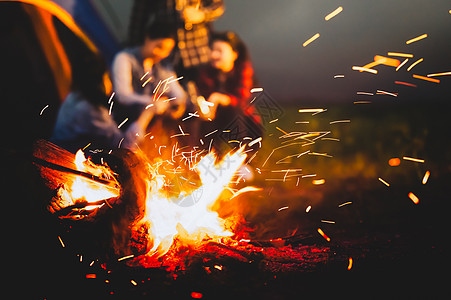 在夏夜背景下 与游客一起点燃篝火 坐在森林露营帐篷附近明亮的篝火旁 一群学生在户外生火 旅行活动和长假周末 朋友们 假期图片