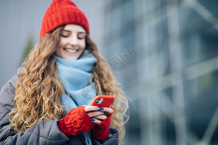 心情愉快的快乐女性在户外的智能手机上打字和滚动 使用智能手机的卷发女性站在外面 一位微笑的快乐女员工在手机上打字 冬天的概念图片