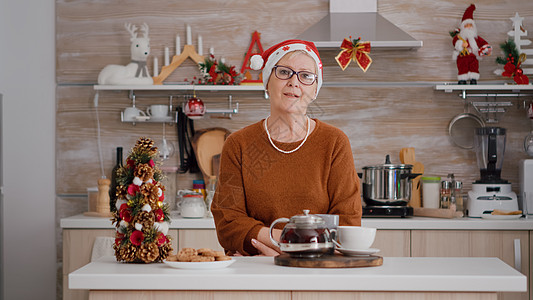 身戴圣塔帽的年长妇女肖像 站在Xma装饰厨房的餐桌前 家庭 帽子图片