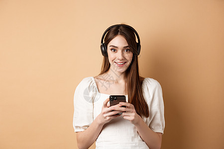 戴耳机的漂亮女孩对着相机微笑 听音乐和使用手机应用程序 蜜蜂背景等 现代的 时髦的背景图片