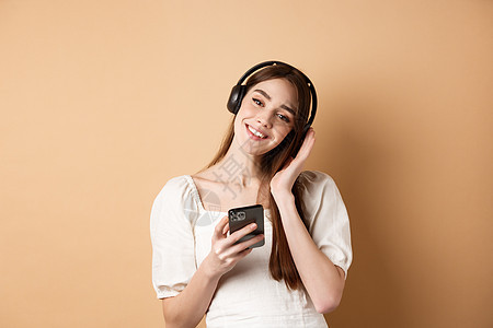 用智能手机 站在蜜蜂背景上用无线耳机监听音乐的可爱笑笑女孩 时尚 假期图片
