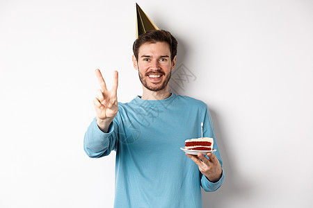 欢庆和节假日概念 快乐的年轻人庆祝生日 用和平标志拍照 戴党帽 并举着白蛋糕 白背景饼等活动 广告 男人图片