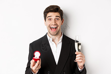 身穿西装的帅帅帅男近身 提出建议 提供订婚戒指和举起香槟杯 站在白色背景下站立 展示 情人节图片