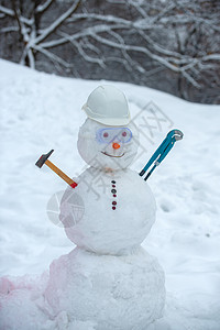 用锤子在雪背景上的雪人工人 在雪原上戴着工作头盔的滑稽雪人 户外雪地里的手工雪人图片