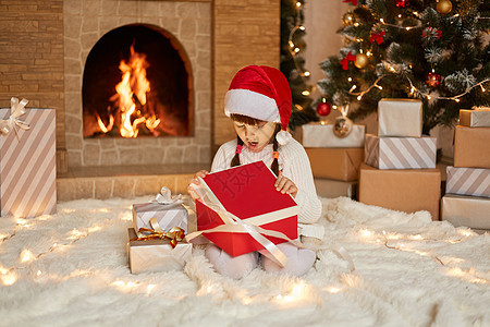 圣诞节儿童在圣诞树附近打开礼物 带着新年礼盒的快乐女婴坐在地板上 脸上带着惊讶的表情 惊讶地发现惊喜图片