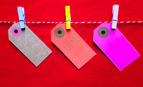 红色背景上的彩色纸币和衣夹 空的彩色纸板价格标签 销售标签 礼品标签 地址标签 挂在衣服上的行李标签 木制夹子 布局 文本复制空图片