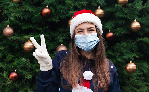 圣诞片 戴着圣诞老人帽子和医用面具的女人情绪激动地特写 以圣诞树为背景 冠状病毒大流行图片