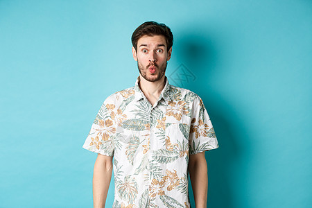 暑假 惊讶的游客说哇 盯着相机 查看很棒的促销 站在蓝色背景中的夏威夷衬衫 商业 成熟背景图片