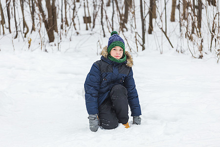可爱的小男孩玩雪 玩得开心 微笑 冬季公园的少年 积极的生活方式 冬季活动 户外冬季运动会 雪球 滚雪球 季节背景图片