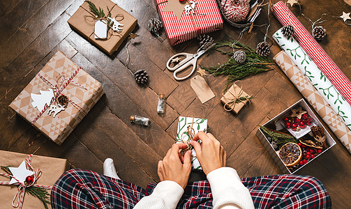 圣诞节装饰元素女人的手包裹着圣诞礼品盒 特写 裁剪过的女性坐在地板上 用装饰元素和物品准备自然生态礼物 圣诞快乐或新年 DIY 包装概念背景