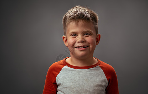 穿着红色衬衫的漂亮学龄前男孩在镜头前微笑 深灰色背景上的快乐孩子 有趣的家庭时光 小男孩在工作室里享受乐趣图片