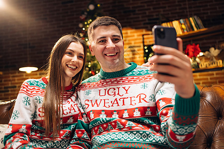 穿着冬日毛衣的情侣在家里录制视频给亲朋好友拜年 使用智能手机与家人交谈的家庭通过视频电话会议应用程序祝贺圣诞快乐图片
