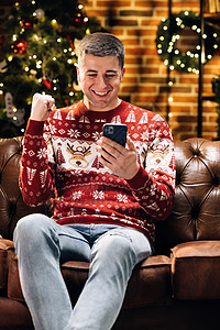 快乐的白种人年轻快乐的男人微笑着惊讶的脸敲打着手机 感到兴奋和快乐赢得圣诞彩票 圣诞节的概念 假期奇迹 圣诞节快乐图片