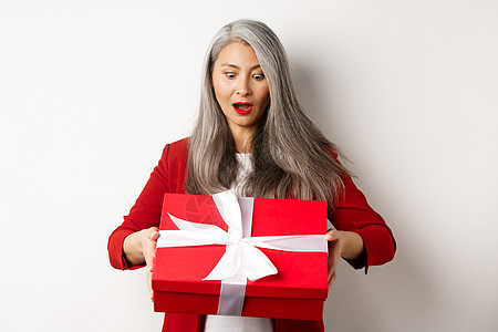 惊讶的亚洲高级女性在母亲节收到礼物 拿着带礼物的红盒子 看起来很惊讶 白色背景 美丽的 商业图片