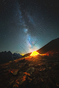 高山上星空的垂直照片 在多山的地平线背景下 饱和的银河指向高山上的一个发光帐篷 天文摄影图片