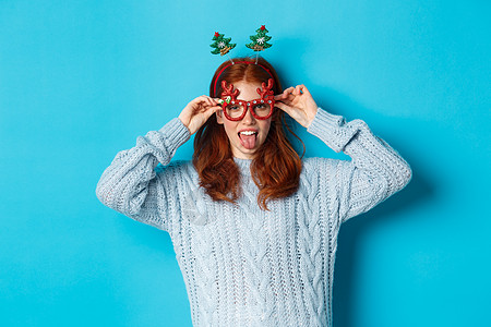 寒假和圣诞节销售理念 庆祝新年的漂亮红发女模特 戴着滑稽的派对头带和眼镜 对着镜头微笑 青少年 有趣的背景图片