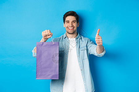 购物 节假日和生活方式的概念 满意的持纸袋微笑的人 展示了拇指和建议商店 站在蓝背景上 笑着 促销 假期胡须高清图片素材
