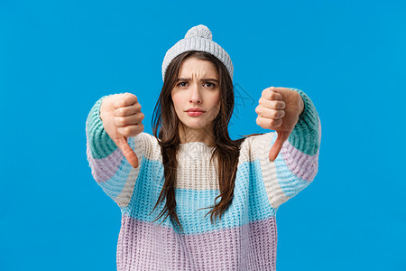 坏主意 不要这样做 穿着冬季毛衣 帽子 表情严肃 心烦意乱的年轻女性 带着判断力 怀疑地做出竖起大拇指的手势 不同意不喜欢某事 图片