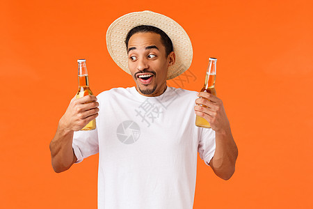 兴奋而快乐 笑得开心的非洲裔美国男性玩得开心 享受休闲 酒店度假 出国旅行 拿着两瓶啤酒 建议喝酒的朋友 站着逗乐的橙色背景图片