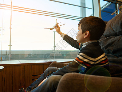 可爱的小男孩拿着玩具飞机伸出手模仿飞行的肖像 在等待航班时 靠着全景窗户俯瞰机场出发航站楼的跑道图片
