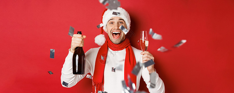 庆祝新年的快乐男人 拿着香槟瓶和杯子 用彩礼顶着红色背景站立在面团上 注 un org/docute_BAR__BAR_ 圣诞节图片