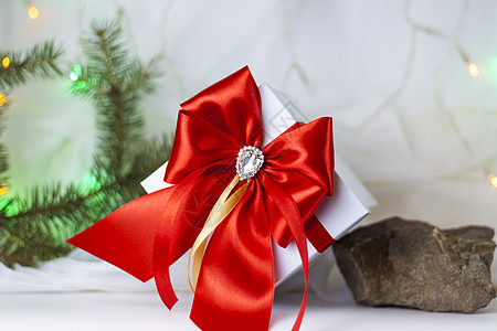 装饰圣诞树一份圣诞礼物 在浅色背景上用冷杉树枝装饰着美丽的蝴蝶结 礼物 喜悦 惊喜 选择性的焦点 圣诞节和新年的概念 手工制作的 庆典背景