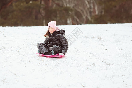 快乐的小女孩滑下山坡 在碟子雪橇上 女孩享受滑滑雪之旅 户外 幸福图片