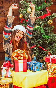 快乐的年轻女人戴着圣诞老人的帽子 在一棵装饰圣诞树的背景下 在一堆礼物中 木背景 特写图片