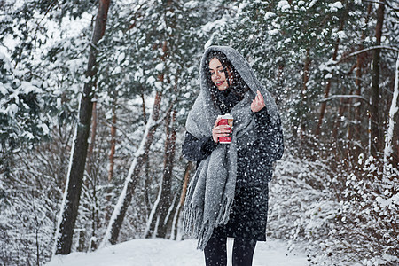 穿着暖身衣的姑娘喝着咖啡 在冬季森林里散步 在寒冬林中散步图片
