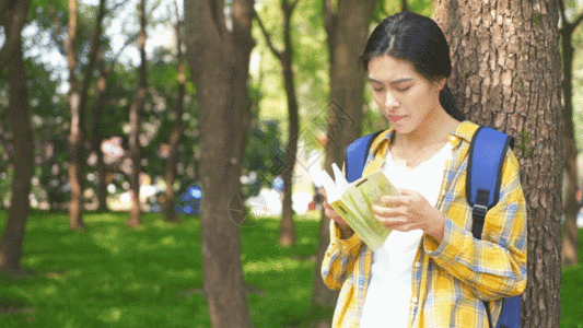 在户外靠在树边看书的女学生GIF高清图片