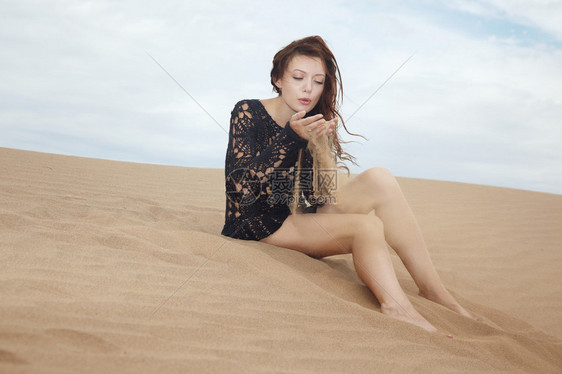 户外女士坐在沙漠中吹着沙粒图片