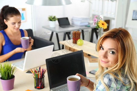 办公室里的两位女设计师喝早茶或咖啡在辛勤工作的一天喝咖啡女员工拿着一杯热饮有创意的人或插画