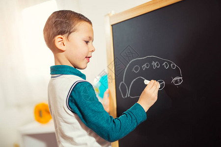 幼稚的涂鸦小男孩在黑板上用粉笔画图片